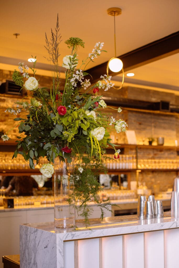 A bright green floral arrangement accented with white and red flowers sitting atop a bar.